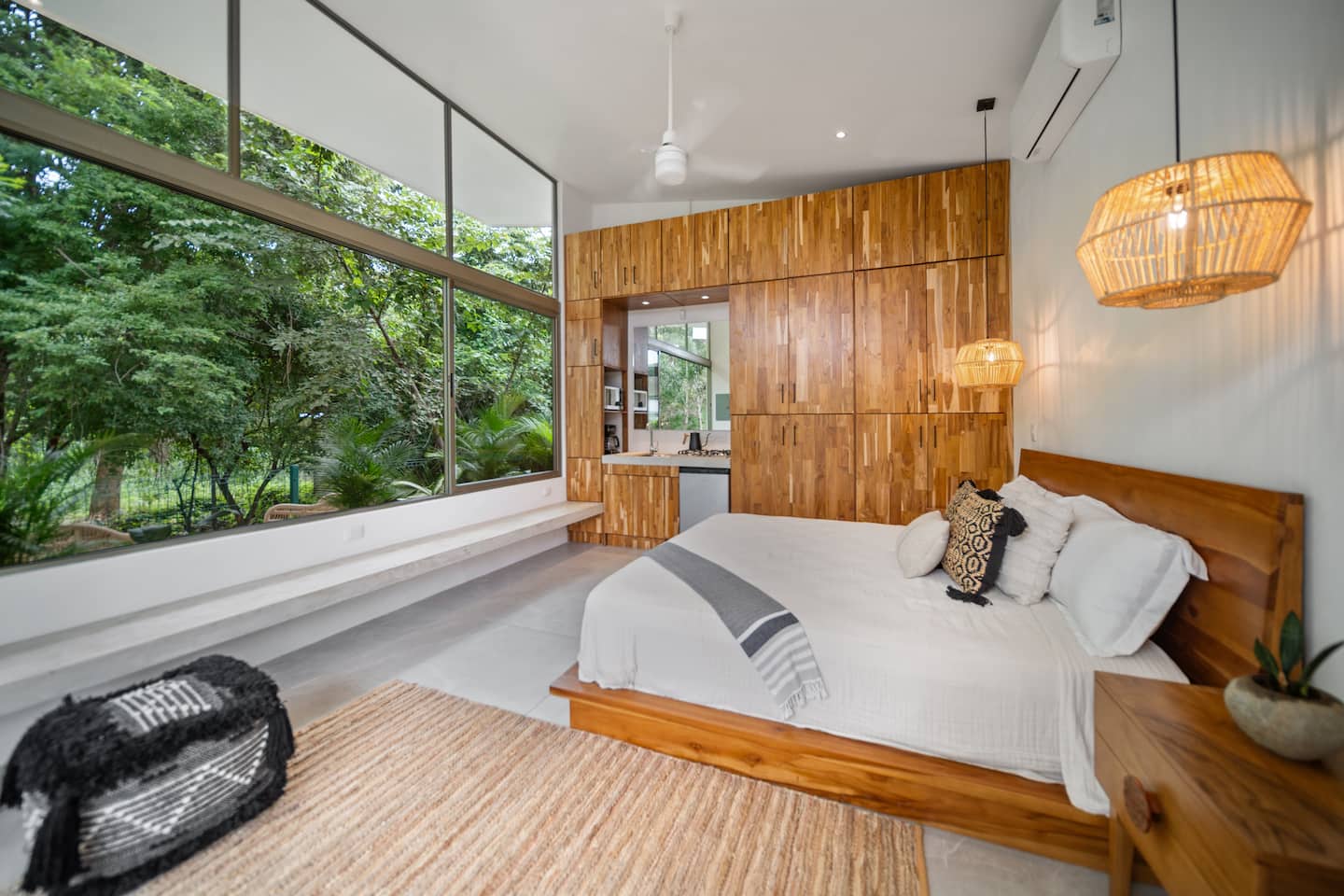 Jungle-view bedroom with teak cabinetry and rattan pendant lights